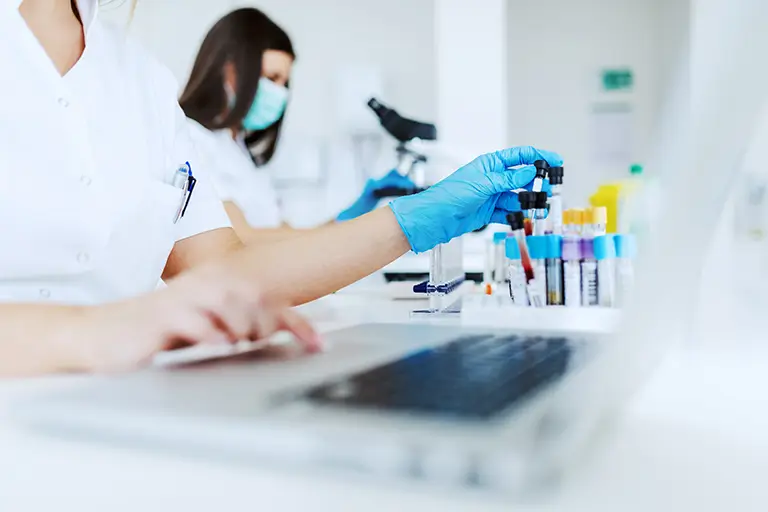 A female scientist in a lab coat typing on a laptop, indicating her involvement in scientific work or experimentation.